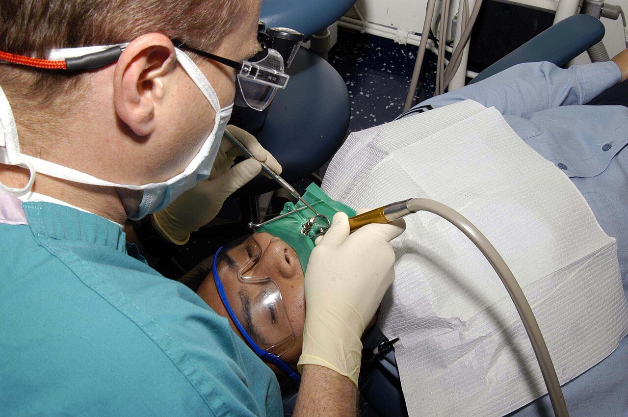 A dentist in scrubs and mask treating a patient