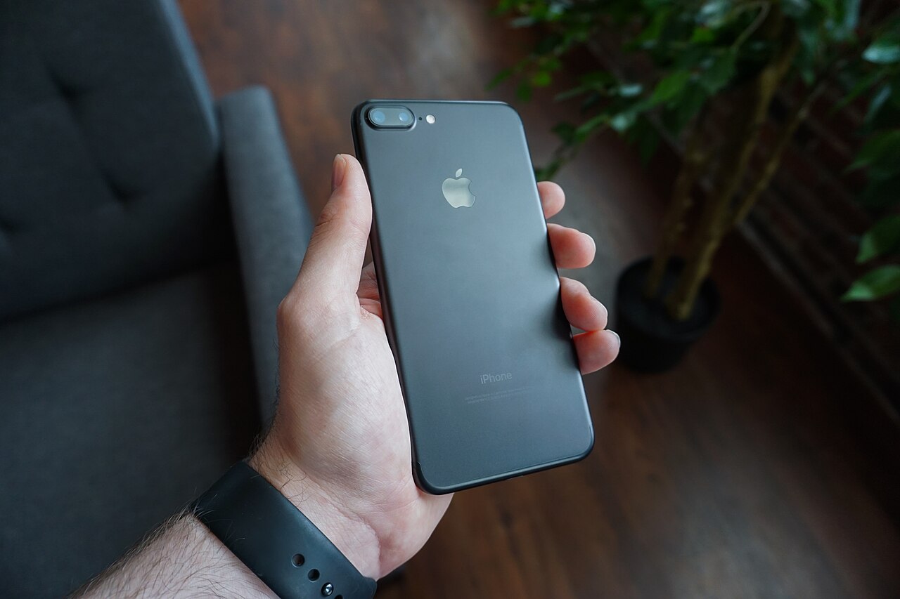 A hand holding a black smartphone showing the camera lens