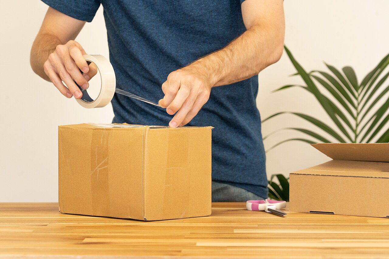 A man sealing a cardboard shipping box with tape