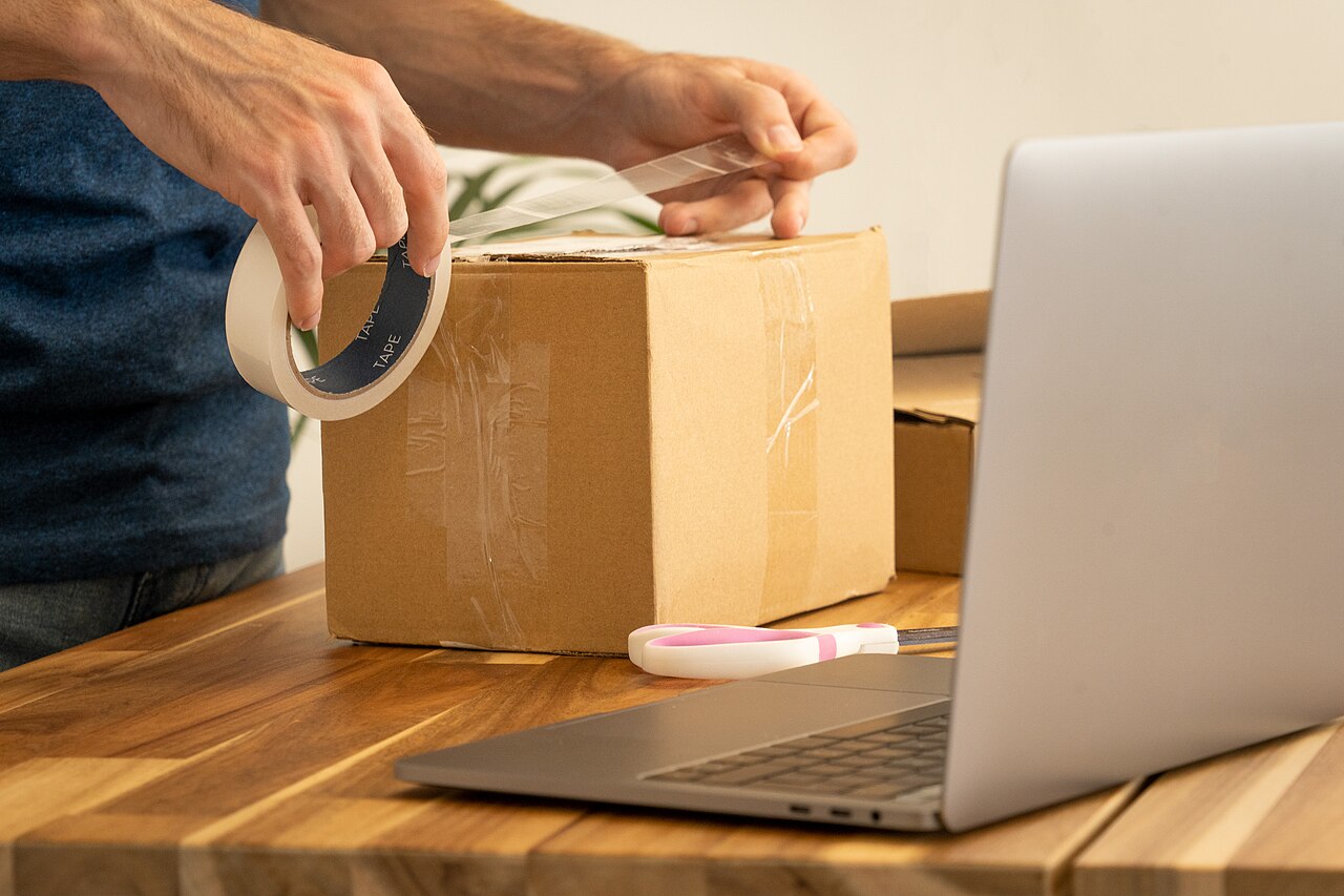 Hands packing a box next to a laptop on a desk