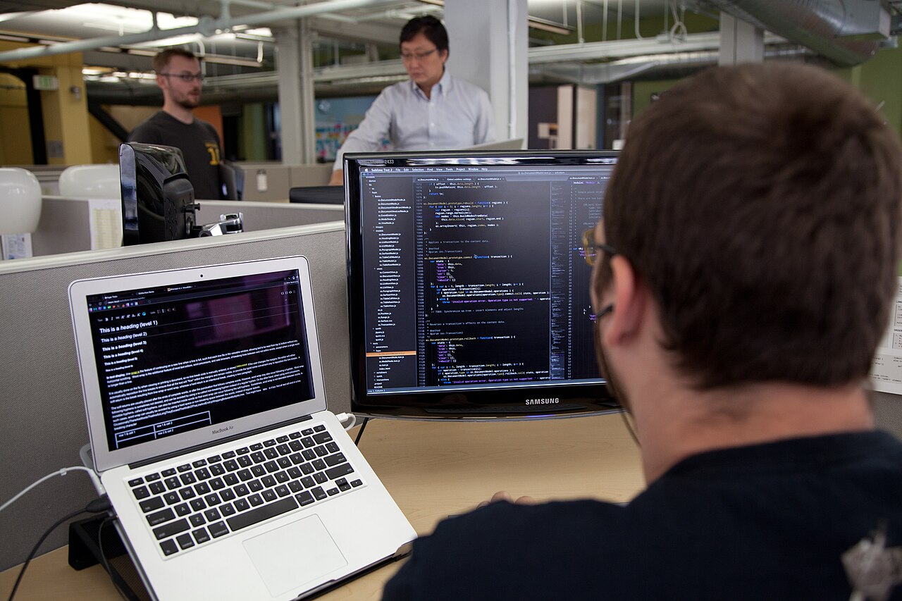 A software developer at a desk with monitors showing code