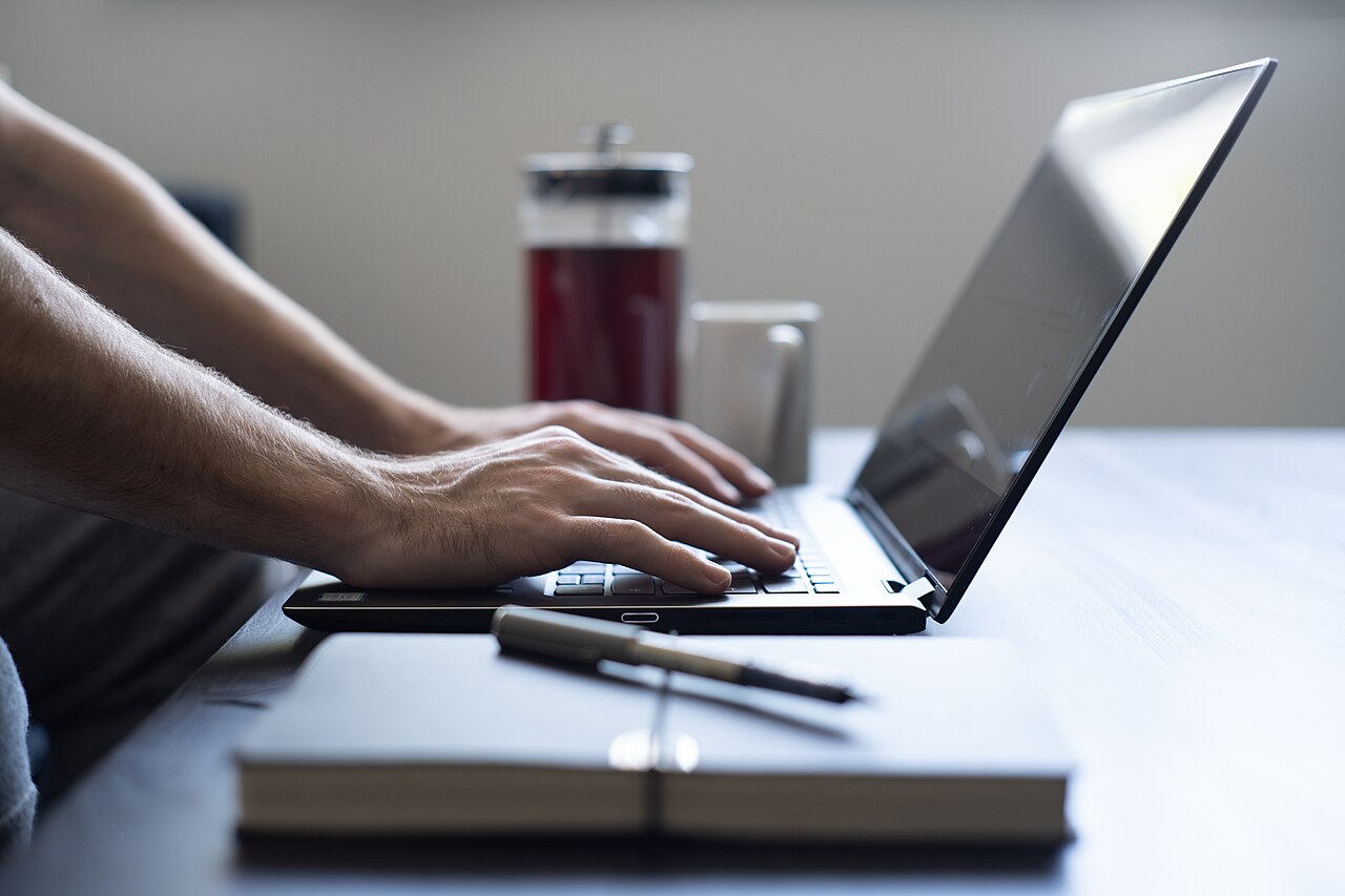 Hands typing on a laptop at a wooden desk
