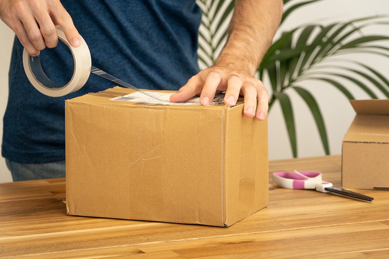 Hands taping a cardboard box for shipping