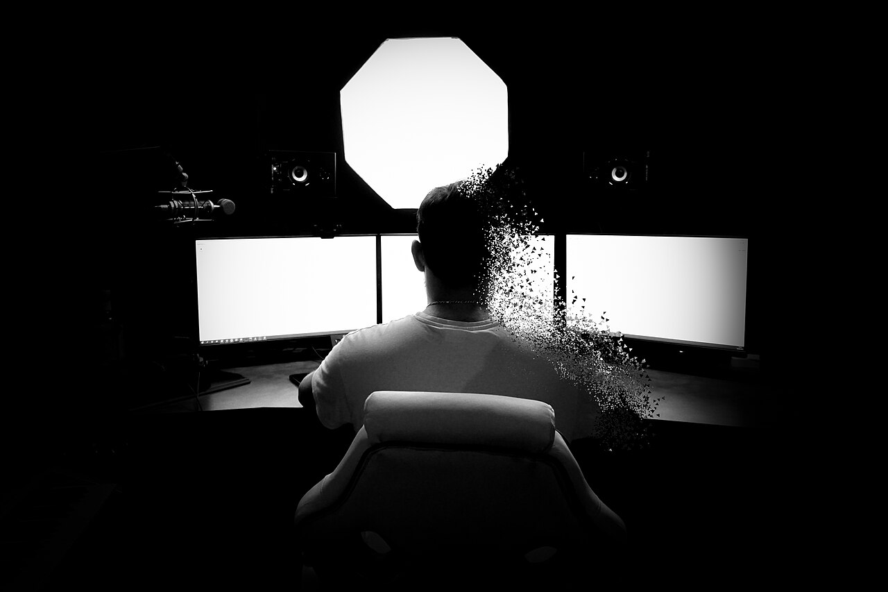 A person working at a multi-monitor desk shown in silhouette
