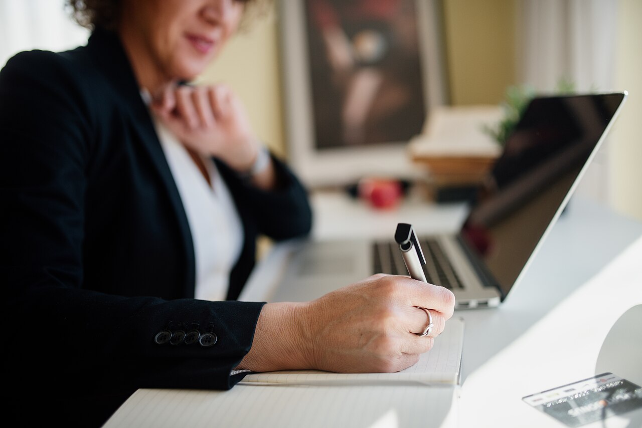 A woman writing in a notebook beside a laptop